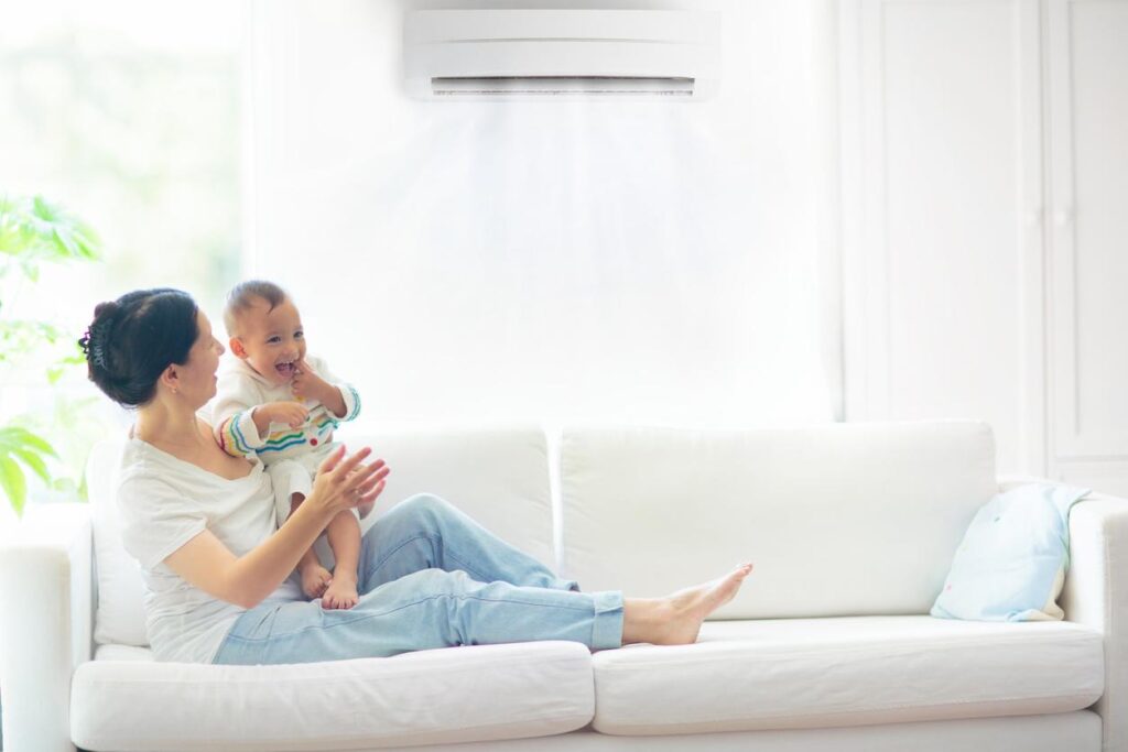 A young mother and baby relaxing on a couch underneath an air conditioner