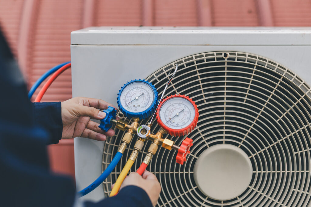 A technician twists the blue valve on a device that is checking an outdoor air conditioning system.